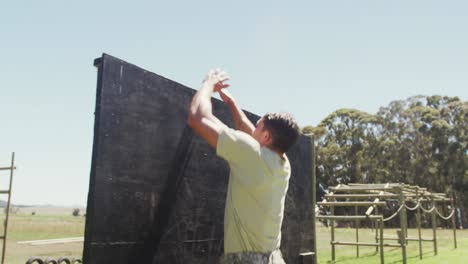 Fit-caucasian-male-soldier-on-army-obstacle-course-in-field-climbing-over-fence-and-running