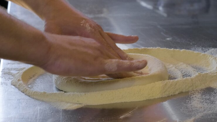 Primo piano di mani che impastano pasta fresca per pizza.