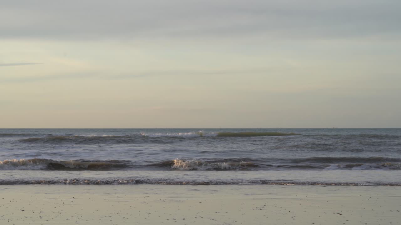 흐린 일몰에 모래 해변에 튀는 파도