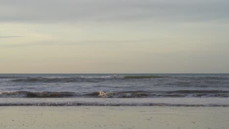 ocean waves splashing on sandy beach on a cloudy sunset