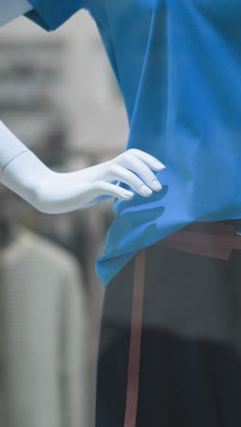 primer plano de un maniquí con una elegante camiseta azul emparejada con un cinturón marrón y pantalones negros, la mano posada en la cadera en la vitrina de una tienda minorista