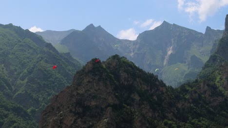 paragliding pilots fly paragliders among clouds and green mountains.