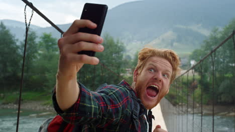 tourist taking selfie smartphone camera closeup. guy making funny face on nature