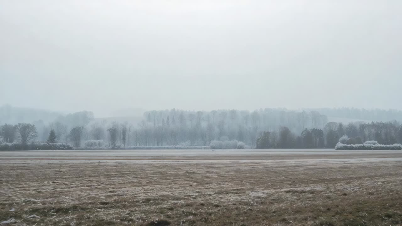 Moving camera passing frosted plowed field at roadside, capturing furrows and misty treeline
