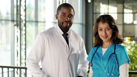 portrait of mixed-race male and female doctors in uniforms smiling joyfully at camera in a clinic