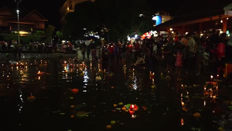 slow motion people pray and put loi krathongs on the water during traditional thai holiday loy krathong in bangkok, thailand. crowd celebrates. river full of beautiful krathongs. 4k