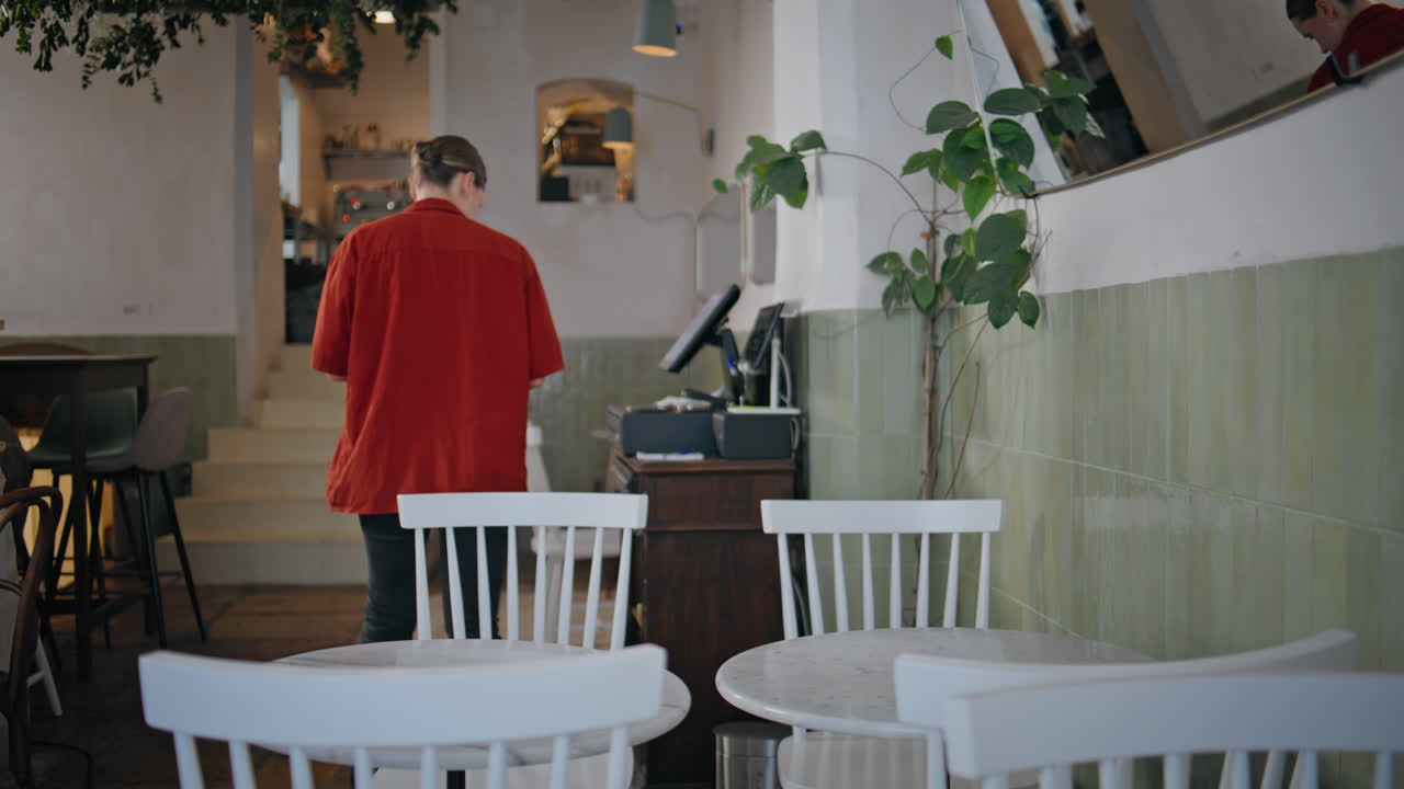 Waitress cleaning cafe table wearing red shirt. Woman wiping surface dining area