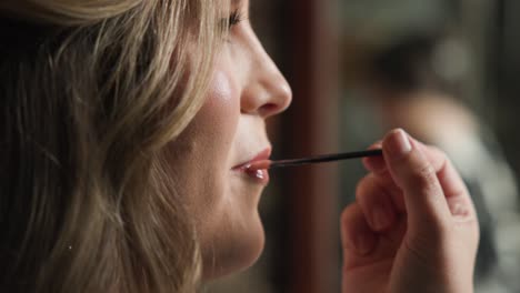 Wedding-Bride-smiling-while-make-up-artist-puts-on-lip-gloss-onto-bride-mouth,-while-being-close-up-and-in-slow-motion