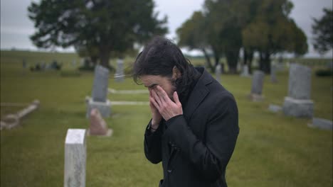 young man in black suit pays respects to the dead in cemetery