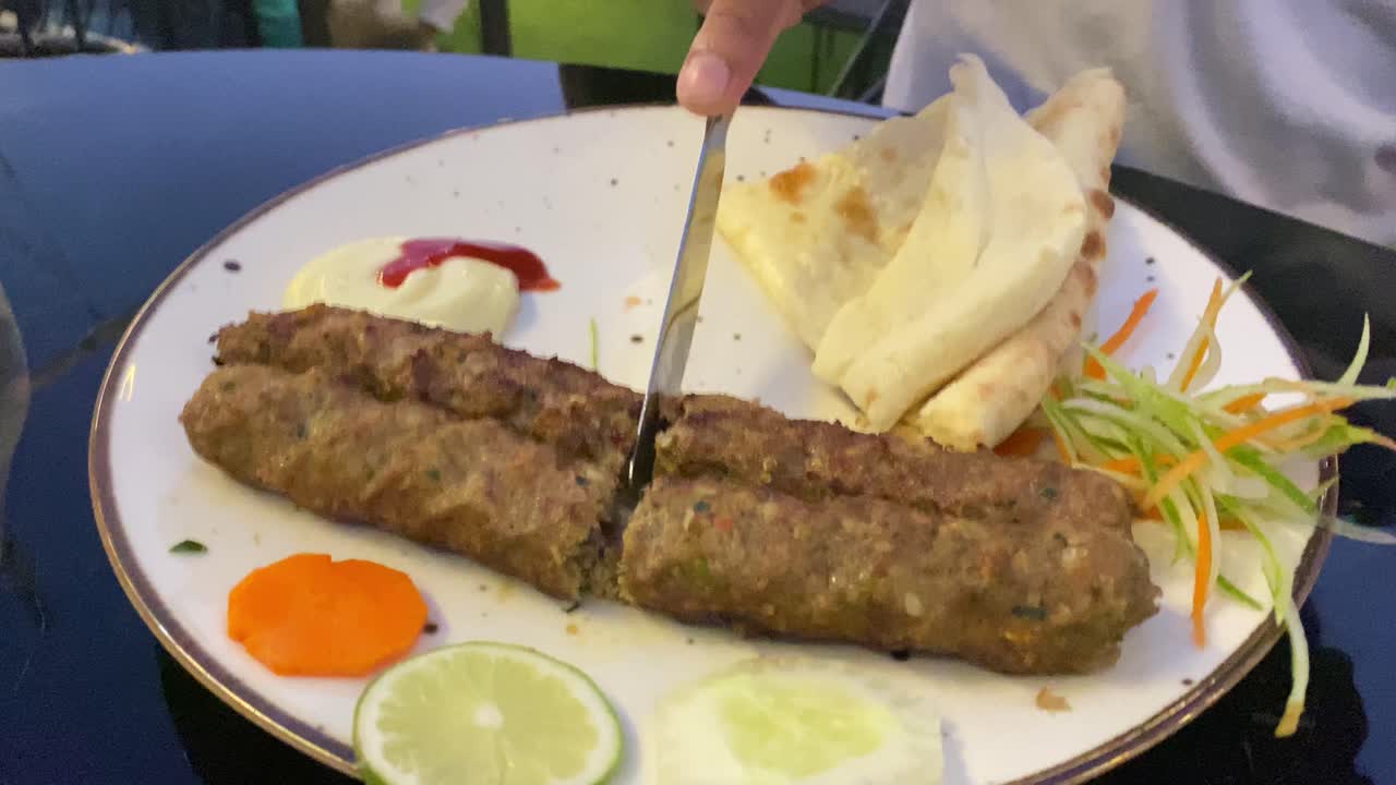 Cortando a mano un delicioso y popular kebab indio con cuchillo de plata y pan plano naan roti suave.