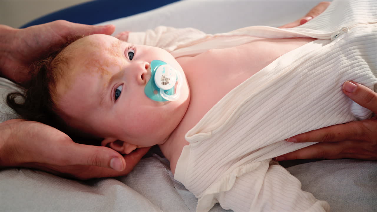 Infant lying relaxed while being supported by the hands of parents