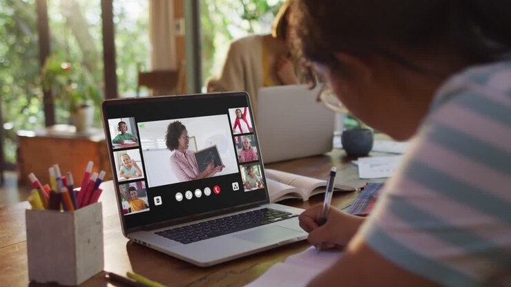 Niña haciendo la tarea y teniendo una videoconferencia con su profesor y compañeros de clase en su portátil en casa.
