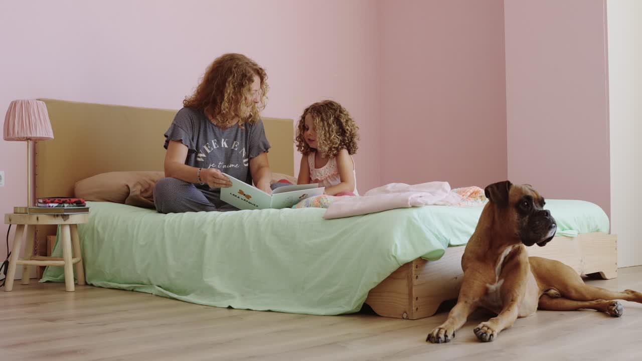 Mother and Daughter Reading on Bed with Boxer Dog