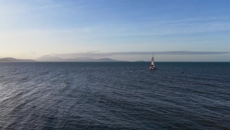 aerial view of a solitary sailing boat navigating calm ocean waters under a serene sunset sky