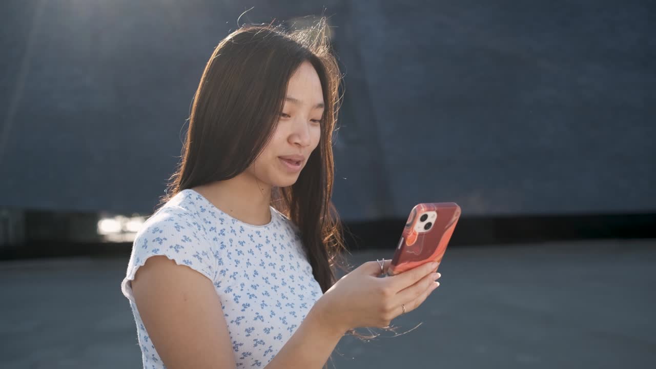 Smiling young Asian woman using her mobile phone while standing outdoors.