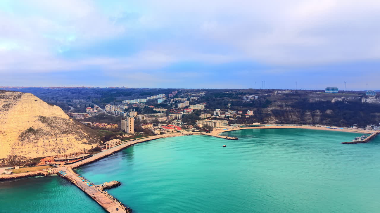 Prospettiva dall'alto di una città costiera con edifici bianchi situata in una baia verde con acqua turchese. Vista aerea di città costiera e baia