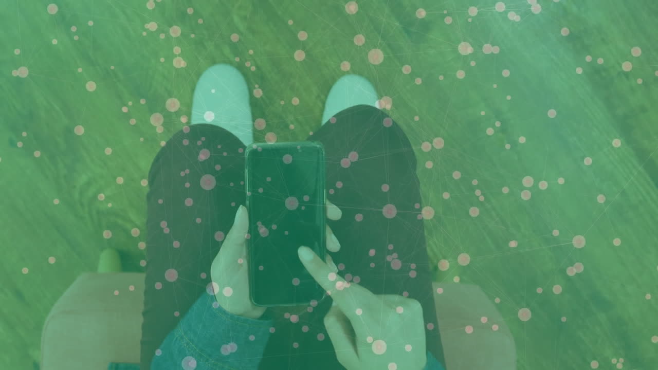 Female user holding smartphone while sitting peach chair, displaying network overlay for technology