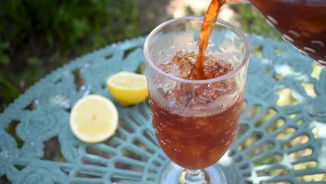 pouring tall glass of ice tea with lemon in outdoor summer garden wind blowing leaves shadows