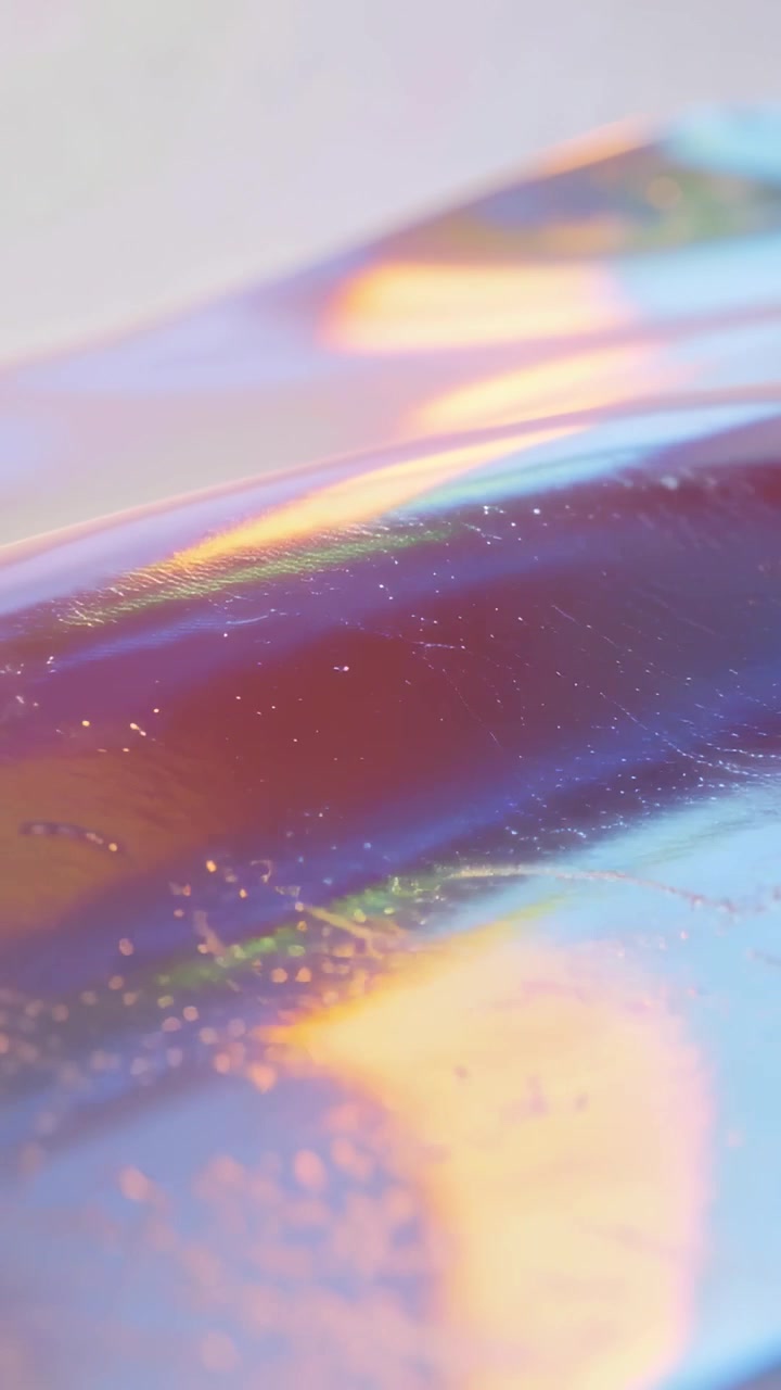Video verticale: Telecamera in panoramica che mostra una pellicola iridescente che riflette bagliori dorati sotto le luci dello studio.