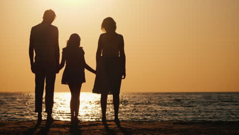 a young family with a child cuddles and looks forward to the sunset over the sea good time together