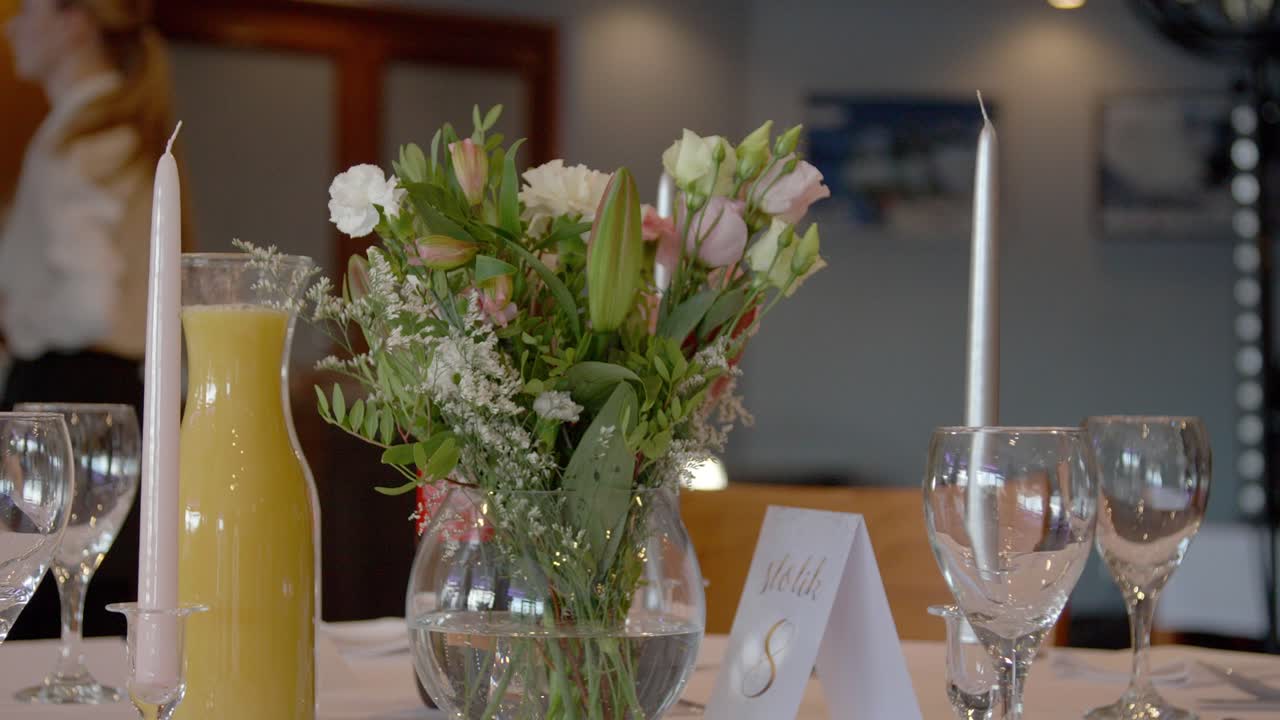 An elegant table prepared for a party with flowers and drinks on it, with a waitress in the background