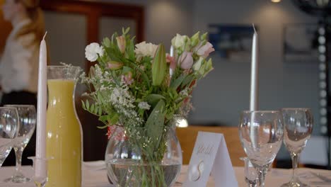 una mesa elegante preparada para una fiesta con flores y bebidas en ella, con una camarera en el fondo