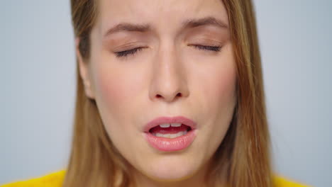 closeup sick attractive woman sneezing at camera on grey background.