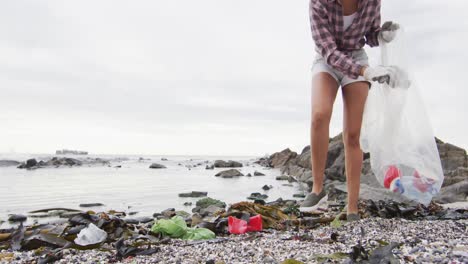 african american woman collecting garbage in a plastic bag at the beach