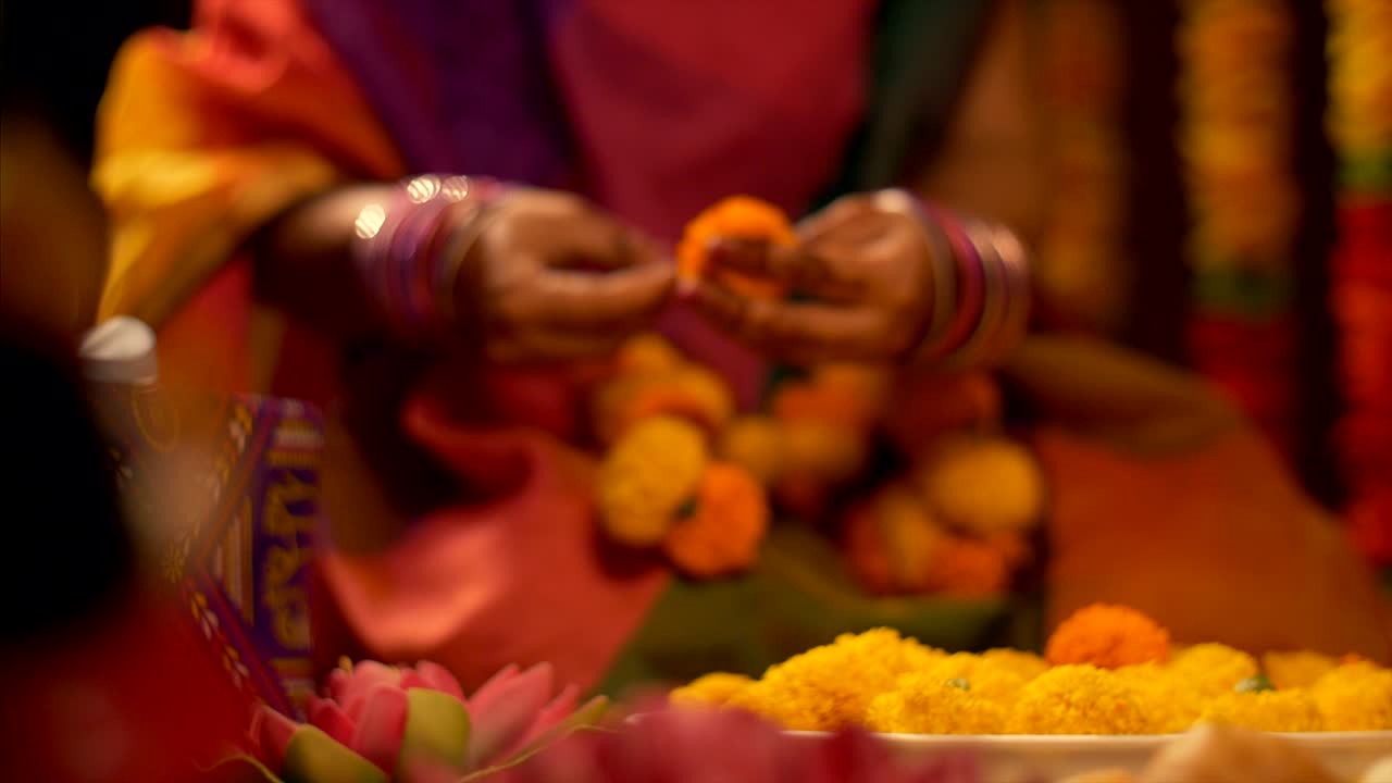 Woman in traditional Indian dress and colorful bangles making the flower garland for diwali puja