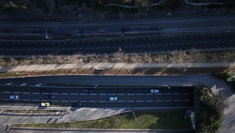 Aerial-flyover-view-of-busy-traffic-driving-rush-hour-highway-with-train-entering-Vallvidrera-tunnel,-Barcelona