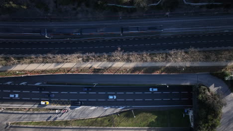 aerial flyover view of busy traffic driving rush hour highway with train entering vallvidrera tunnel, barcelona