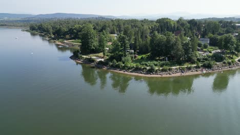 shroreline of calm lake in beskid mountains, surrounded by greenery during a summer day - aerial view 4k