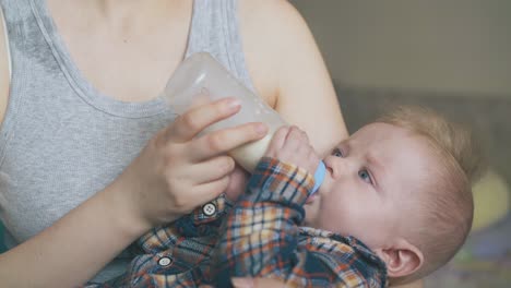 mommy rocks little son eating milk mix from bottle in room