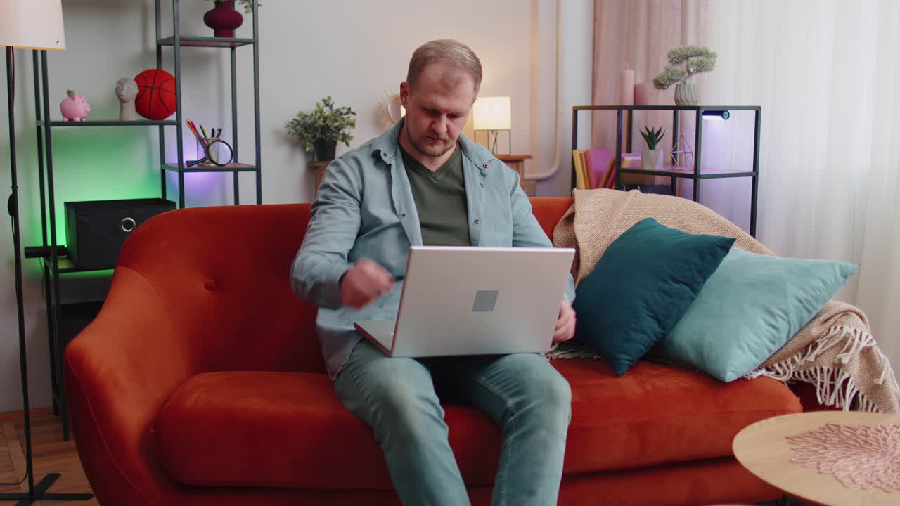 hombre caucásico sentado en el sofá abriendo una computadora portátil comenzando a trabajar aprendizaje electrónico en línea en la habitación en casa