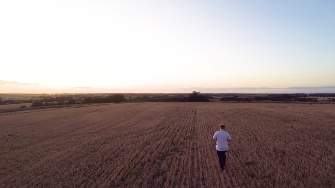 siguiendo lentamente a un hombre que camina por un campo de agricultores antes de ascender para revelar una hermosa puesta de sol de verano