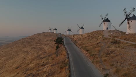 Toma-Aérea-Sobre-Una-Carretera-Cerca-De-Una-Fila-De-Molinos-De-Viento-En-Consuegra,-España