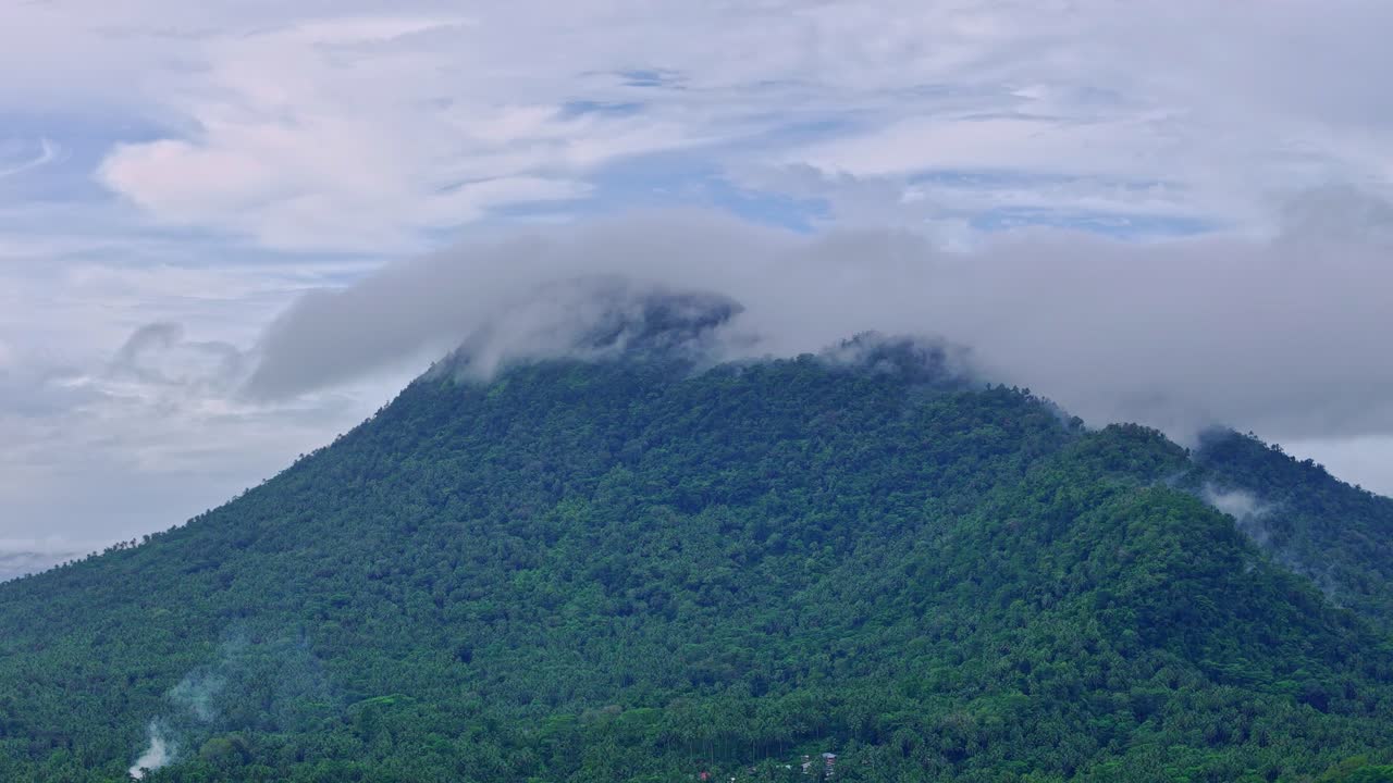 Rekaman udara Gunung Paco di Surigao del Norte, Filipina, yang memperlihatkan medan pegunungan yang tertutup awan dan lereng berhutan. Rekaman drone menangkap detail lanskap alam di bawah kondisi mendung