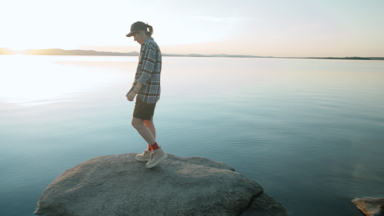 mujer viendo la puesta de sol desde la orilla de un lago rocoso