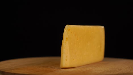 fast rotation of piece of yellow cheese with holes on wooden board on black background.