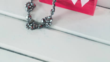 animation of pink jewellery pink box, ribbon and necklace on white wooden background