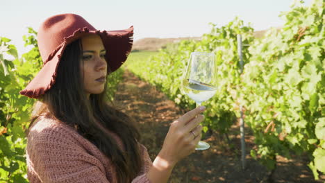 woman in a vineyard looking at a glass of wine