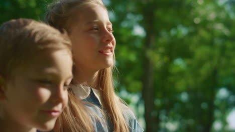 two smiling kids stand lookin in distance. blond siblings hugging close up.