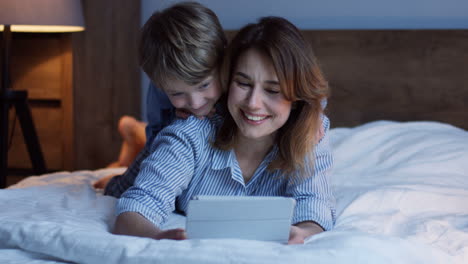 Mujer-Caucásica-Encantadora-Haciendo-O-Viendo-Algo-En-La-Tableta-Mientras-Su-Hijo-Pequeño-Mira-Por-Encima-Del-Hombro