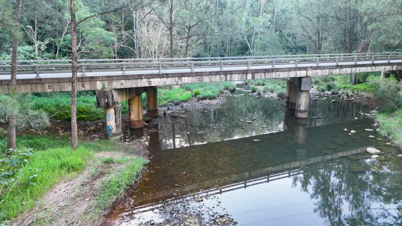 Aerial footage captures a tranquil creek with a bridge in lush bushland, showcasing natural beauty and calmness