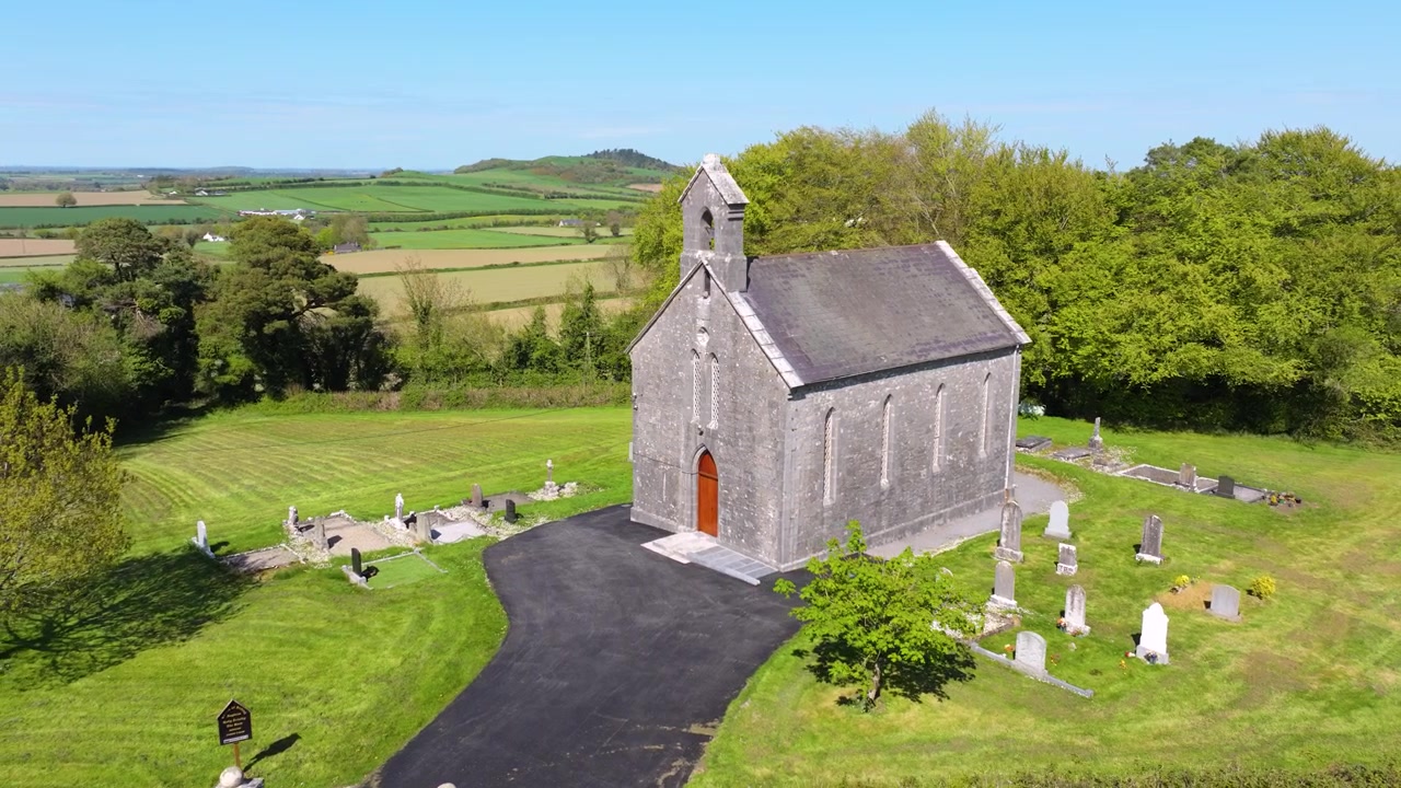 Et historisk stenkapel er omgivet af gamle gravsten og frodigt grønt i County Laois, Irland. Ideel til kulturarvsdokumentarer eller rejseindslag.