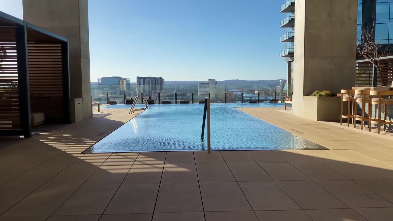 A rooftop infinity pool reflects the clear blue sky, with Austin's skyline in the background. Ideal for urban lifestyle or luxury travel content.