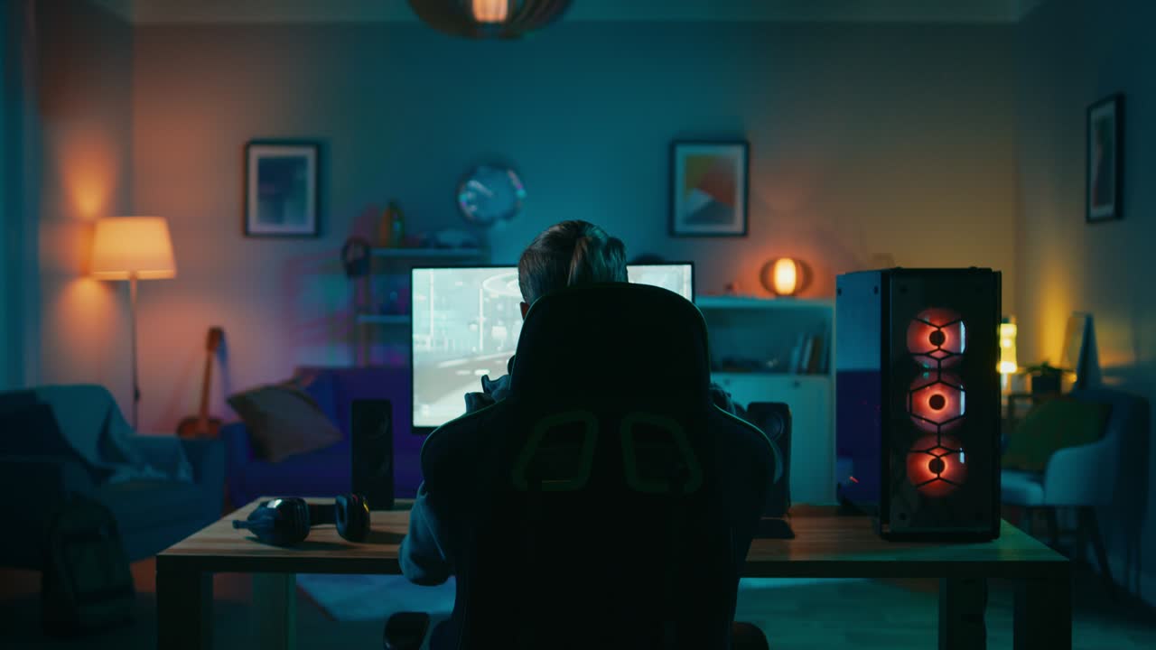 그의 강력한 개인 컴퓨터에서 1인칭 슈팅 온라인 비디오 게임을 플레이하고 승리하는 게이머의 뒷면.방과 pc에는 다채로운 네온 led 조명이 있습니다.집에서 편안한 저녁.