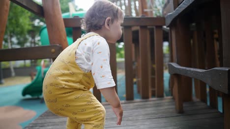 an adorable baby girl toddler playing and climbing on an outdoor playground set - slow motion