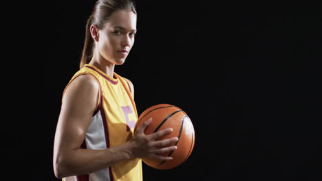 confident young caucasian woman holds a basketball on a black background, with copy space