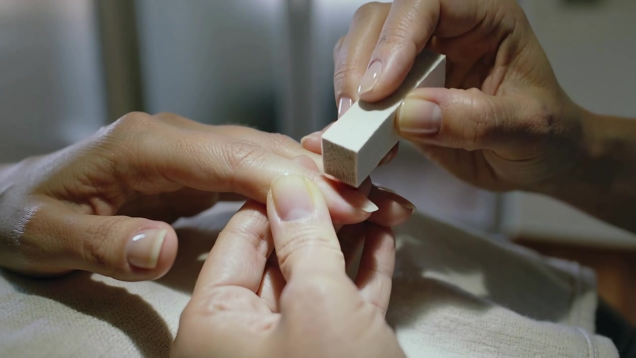 Nail technician placing white buffer onto client nail on folded towel at salon, smoothing free edge